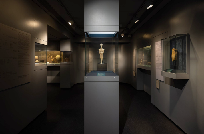 Central Cycladic female figurine surrounded by other marble artifacts at Museum of Cycladic Art in Athens.