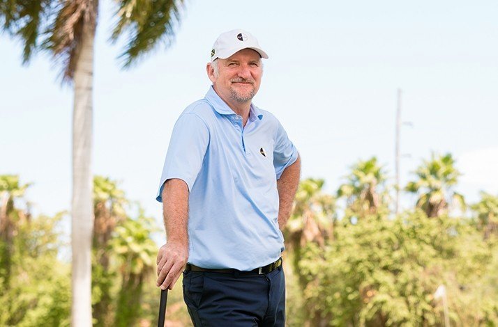 A man wearing a white cap standing on a golf court ready for the game.