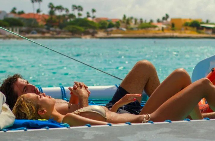 A man and woman are laying on a catamaran at Palm Beach, Aruba. 