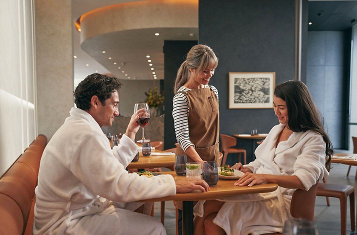 A couple with robs sitting on a table with glasses of wine and looking at the menu in the restaurant of the spa