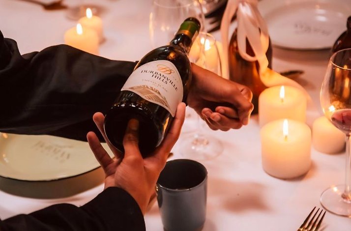 Hands holding a bottle of Durbanville Hills wine at a table decorated with white candles.
