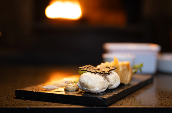 Dusted puff pastries with cream and a dark leaf tuile served on a slate platter before a warm fireplace.