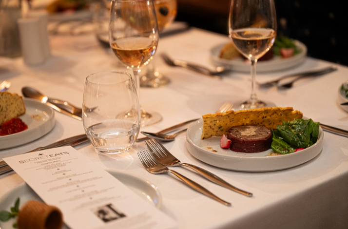 Close-up of a plated meat terrine served alongside crispy herb flatbread, spinach, and radishes.