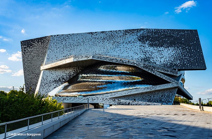Angular mirrored building with sculpted opening under blue sky, viewed from a plaza. Credit: Marco Borggreve