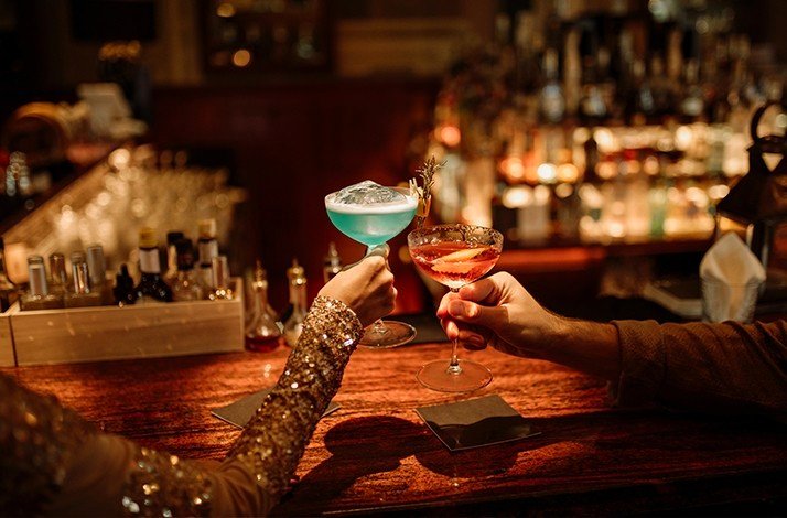 A man and a woman clinking cocktails at Aruba's Boutique Speakeasy.