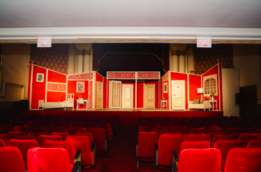 Grand theater stage with red seats and a classic set design, ready for a live performance.
