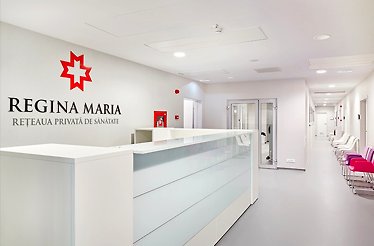 A bright, modern clinic interior featuring a white corridor and reception area, with clean design and the red REGINA MARIA logo visible, creating a professional and welcoming healthcare environment.