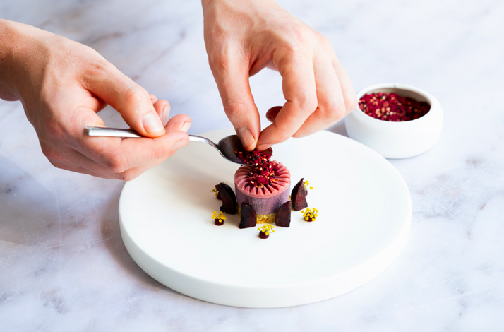 Chef plating a gourmet dessert with red and yellow garnish on a white plate.