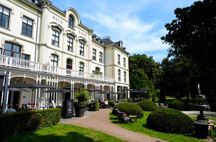 Elegant Hotel Villa Ruimzicht exterior with garden, fountain, and terrace seating.