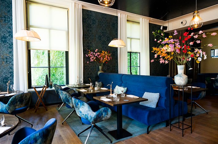 Hotel Ville Ruimzicht restaurant with blue seating, floral decor, and set tables.