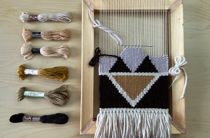 top view from a loom with a fabric halfway up, with some threads of different colors next to it