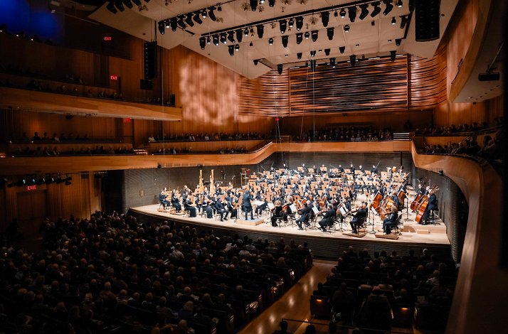 New York Philharmonic orchestra playing on the stage for fully booked auditorium.
