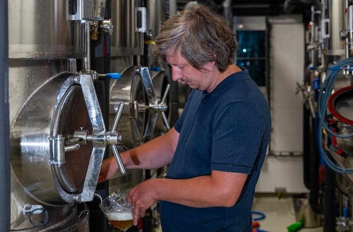 A man trying a beer of various stages of aging directly from the tank.