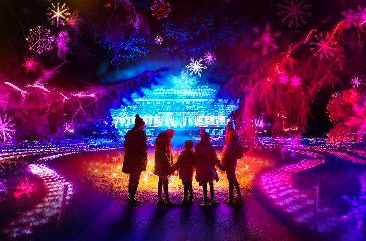 Four visitors standing near the Kew Gardens,  illuminated for the Christmas season