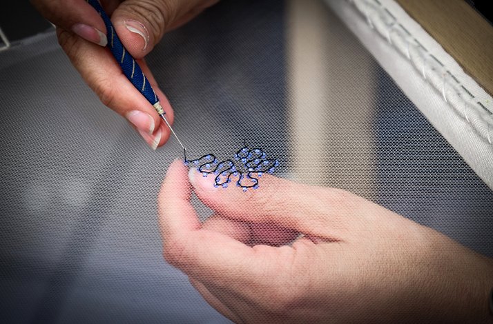 A close-up of woman’s hands holding a needle and embroidering a pattern on canvas at the Pino Grasso Ricami atelier.