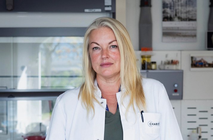 Navena Widulin, wearing a white Charité lab coat in a laboratory setting.