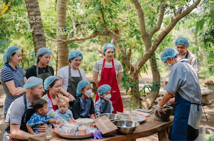 A adult teaching to a group of persons how to use a mortar