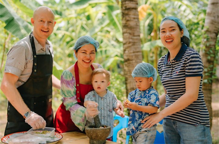 A group of adults cooking with some children who are using a mortar