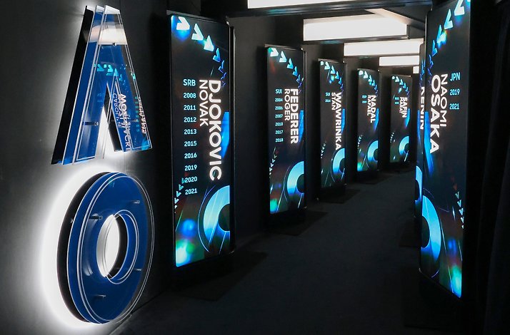 A hallway featuring a blue AO sign and vertical illuminated screens displaying tennis champion names and years.