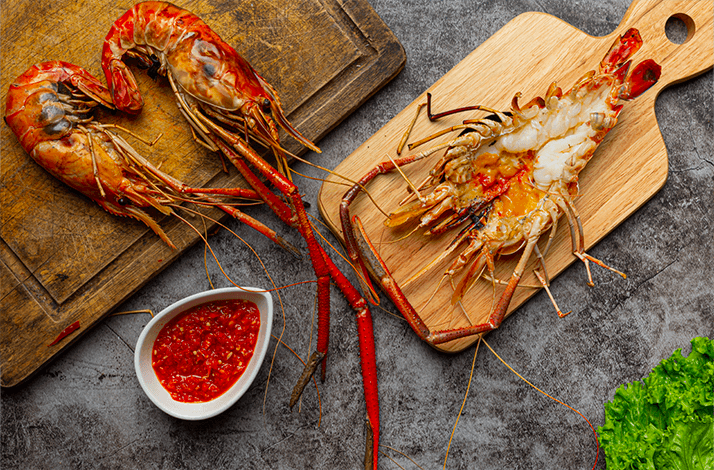 Grilled giant river prawns served with sauce on wooden boards in Thailand.