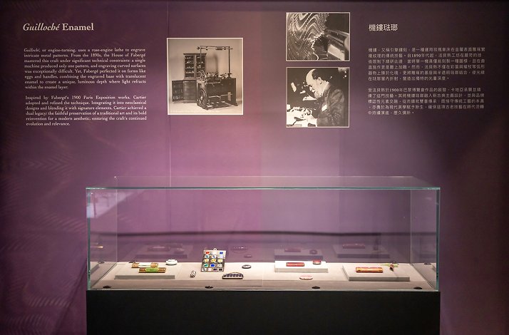 An exhibition display at Liang Yi Museum featuring a glass case of guilloché enamel objects under wall text about Fabergé and Cartier’s techniques.