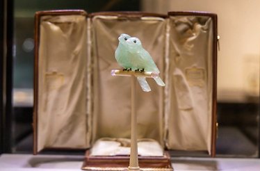 Two pale green hardstone lovebirds by Fabergé, perched on an ivory and pink chalcedony stand, with their original leather display box behind.
