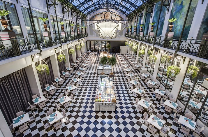 A bright dining hall with a glass ceiling and checkered floor set for breakfast