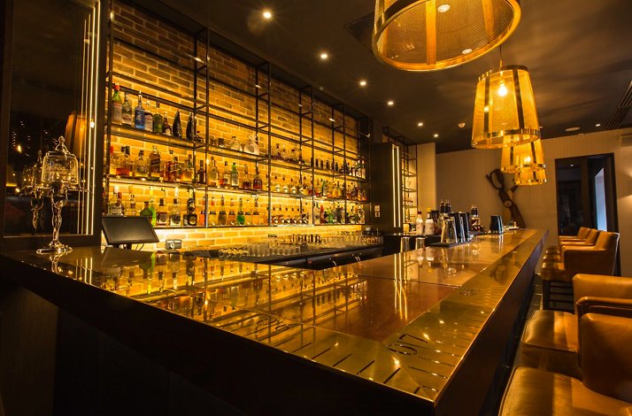 A stylish bar with a polished counter, leather chairs, and shelves of liquor bottles against a brick wall