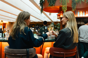 Two women toasting with champagne at a modern bar counter at Hotel V.
