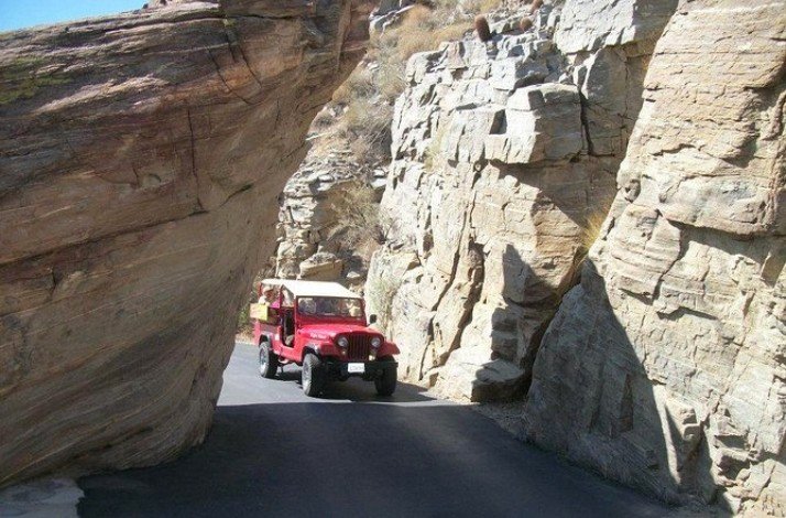 A red jeep rides through Indian Canyon between the rocks.