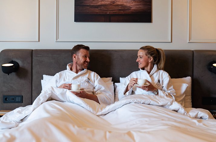 A couple drinking tea in a master bed at Hotel Flora Batava.