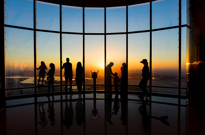Visitors enjoying the sunset view of the city through panoramic windows At the Top, Burj Khalifa.