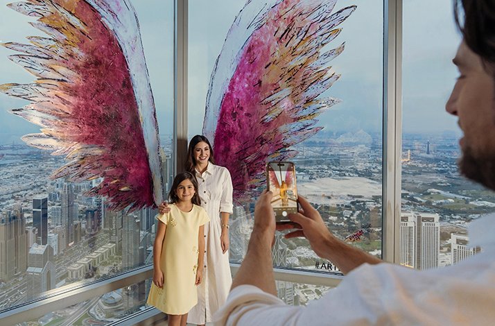 Happy family take a photo At the Top, Burj Khalifa with colorful wings on the panoramic window.