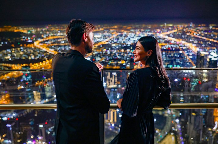 A couple chats sweetly against the backdrop of the city lights at night At the Top, Burj Khalifa.