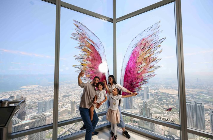 Happy family take a photo At the Top, Burj Khalifa with colorful wings on the panoramic window.