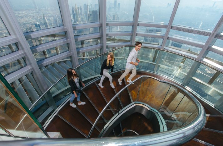 Two girls and a guy climb the circular staircase At the Top, Burj Khalifa.