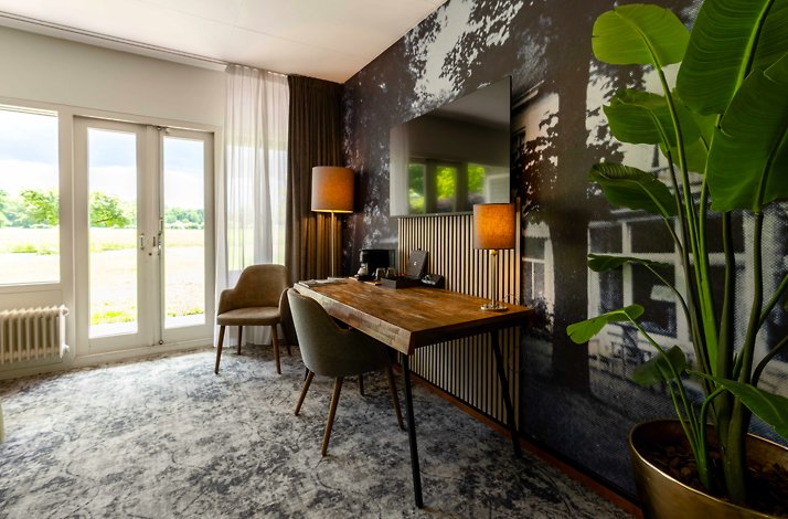 Stylish hotel room desk area with wooden table, upholstered chairs, and countryside views through French doors at Hotel Carelshaven.
