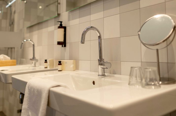 Modern hotel bathroom with white sinks, chrome faucets, toiletries, and a vanity mirror at Hotel Carelshaven.