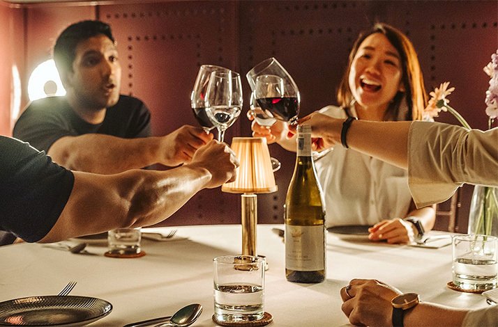 Four guests raising glasses having a toast with wine.