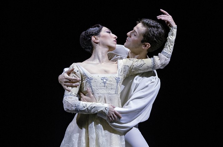 Two performers in period costumes dancing an intimate duet on stage.