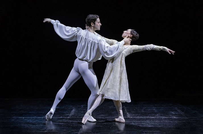 Two ballet dancers perform a dramatic duet on stage, dressed in period costumes under theatrical lighting.