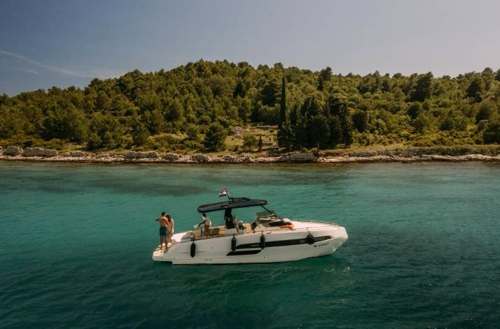A shot of the yacht in the water with a forest on the shore.