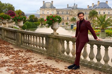 A man wearing a burgundy suit from Two Tailor and posing on the terrace.