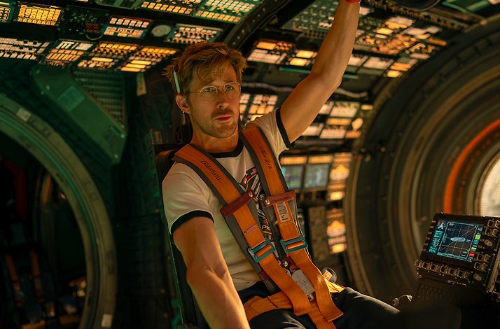 Ryan Gosling visibly focused and concerned, surrounded by illuminated control panel in soft yellow light