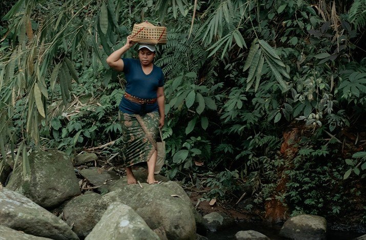 farmer's wife standing and holding a basket overhead in bali indonesia