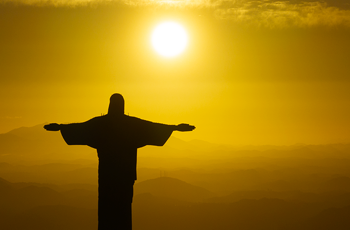 Christ the Redeemer statue silhouetted against a sunrise sky. 