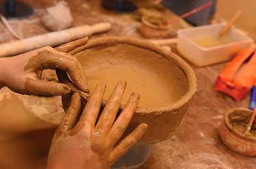 A close up of hands working with clay to shape a dish.