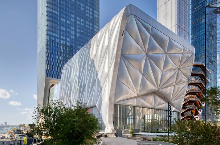 An exterior view of The Shed building, featuring a complex, alongside other high-rise structures in the cityscape