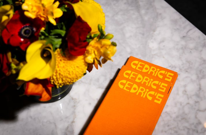 An orange book with the name Cedric's next to a flower pot