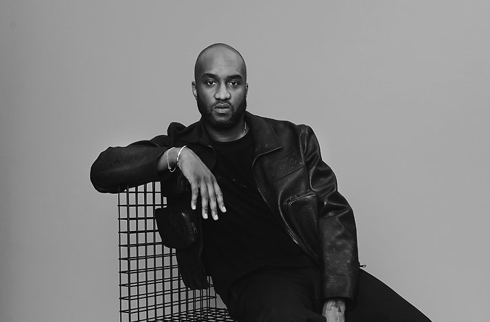 Black and white studio portrait of fashion designer Virgil Abloh sitting on a black grid chair.